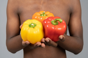 A shirtless young man holding bell peppers