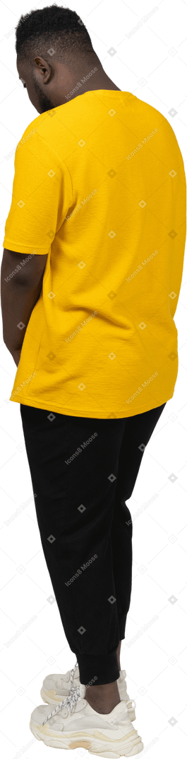 一个身穿黄色 t 恤、摸着肚子、往下看的黑皮肤年轻男子的四分之三后视图