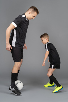 In voller länge von einem jungen mann, der einem kleinen jungen beibringt, wie man fußball spielt