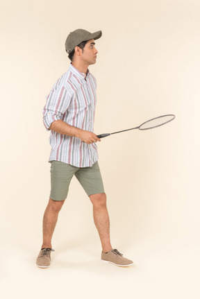 Young caucasian guy standing in profile and holding tennis racket