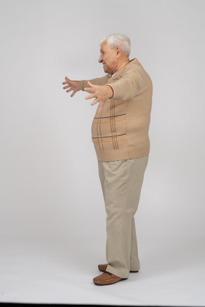 Side view of a happy old man in casual clothes standing with outstretched arms