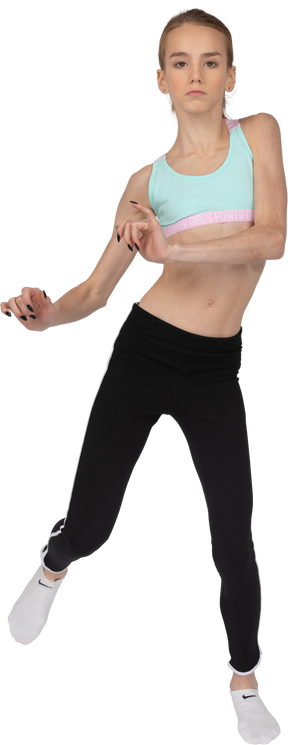 Vista frontal de uma adolescente em roupas esportivas, levantando as mãos e a perna enquanto dançava