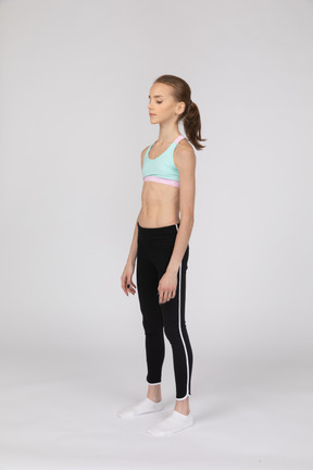 Three-quarter view of a teen girl in sportswear standing still and looking down