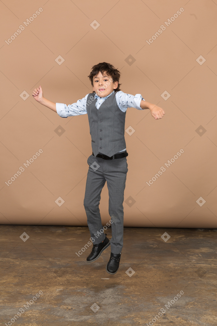 Vista frontal de un chico lindo en traje saltando con los brazos extendidos
