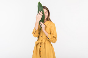 Young woman closing her face with green leaf with eyes closed