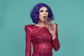 Drag queen en robe à paillettes roses buvant un verre dans une tasse en plastique