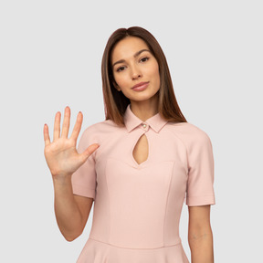 A young woman in a pink dress making a stop sign