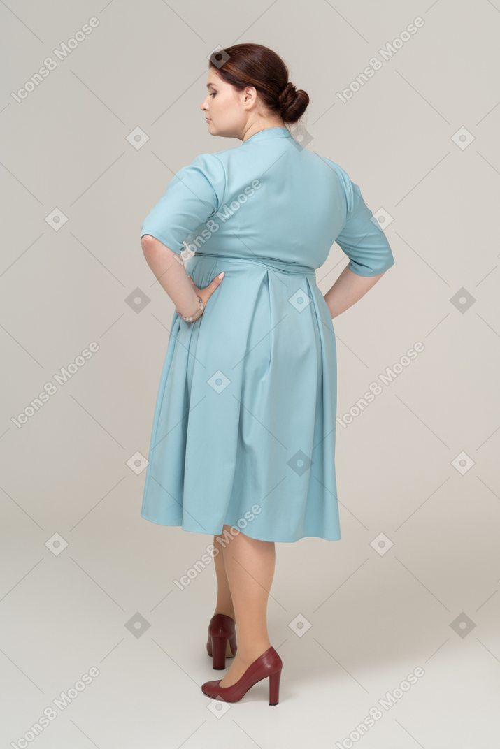 Vista posteriore di una donna in abito blu in posa con le mani sui fianchi