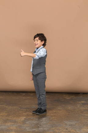 Vista lateral de um menino de terno cinza, aparecendo o polegar
