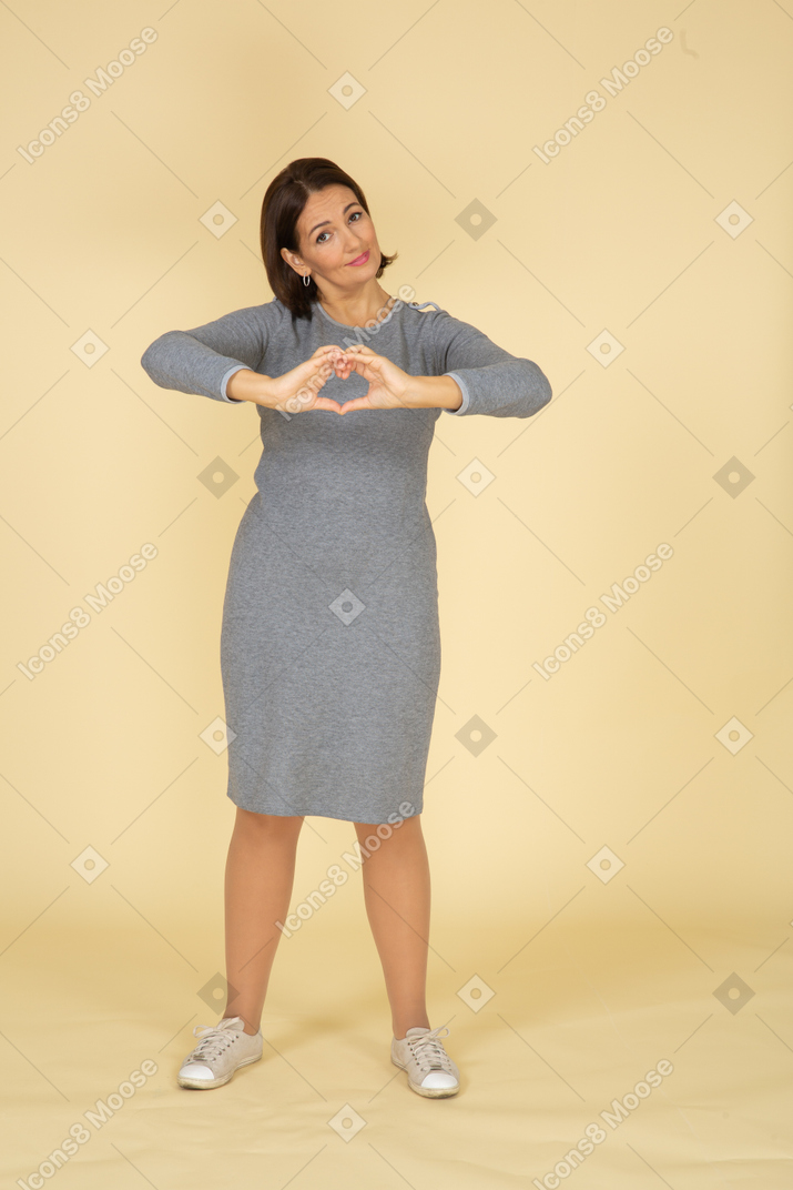 Front view of a woman in grey dress showing heart gesture