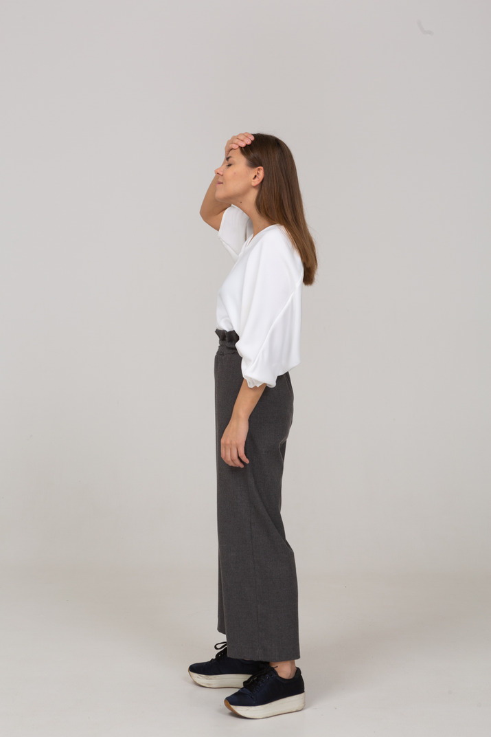 Side view of a young lady in office clothing touching forehead