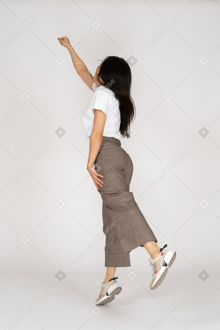 Dreiviertel-rückansicht einer springenden jungen dame in reithose und t-shirt, die ihre hand ausstreckt
