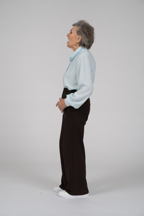 Вид сбоку на пожилую женщину в формальной одежде, гримасничающую и зевающую влево