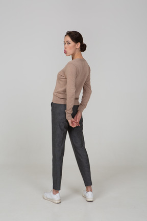 Vista posteriore di tre quarti di una giovane donna in pullover e pantaloni che mostra la lingua