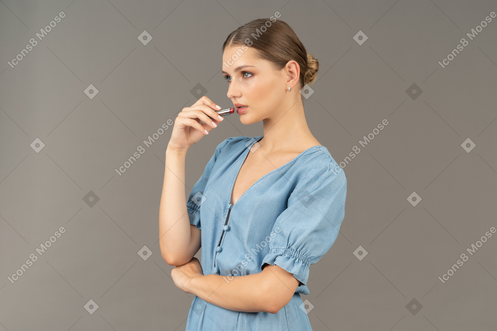 Three-quarter view of a young woman in blue dress applying a lipstick