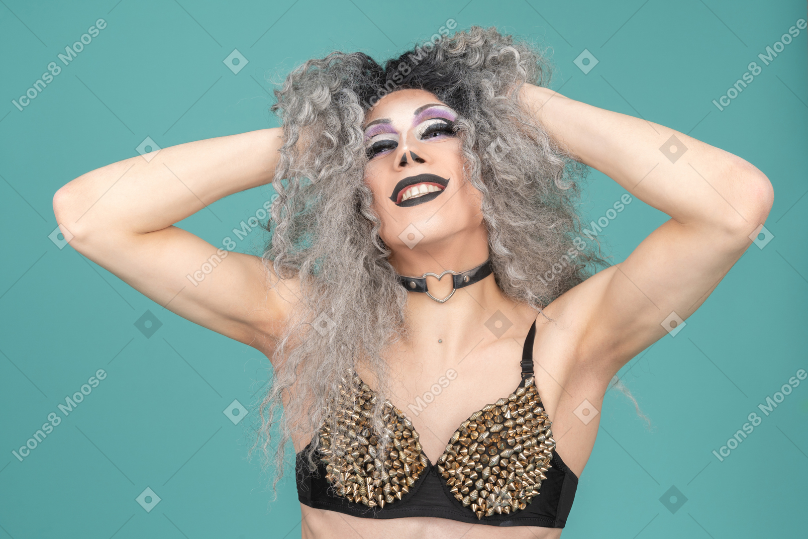Drag queen in studded bra smiling with hands in their hair