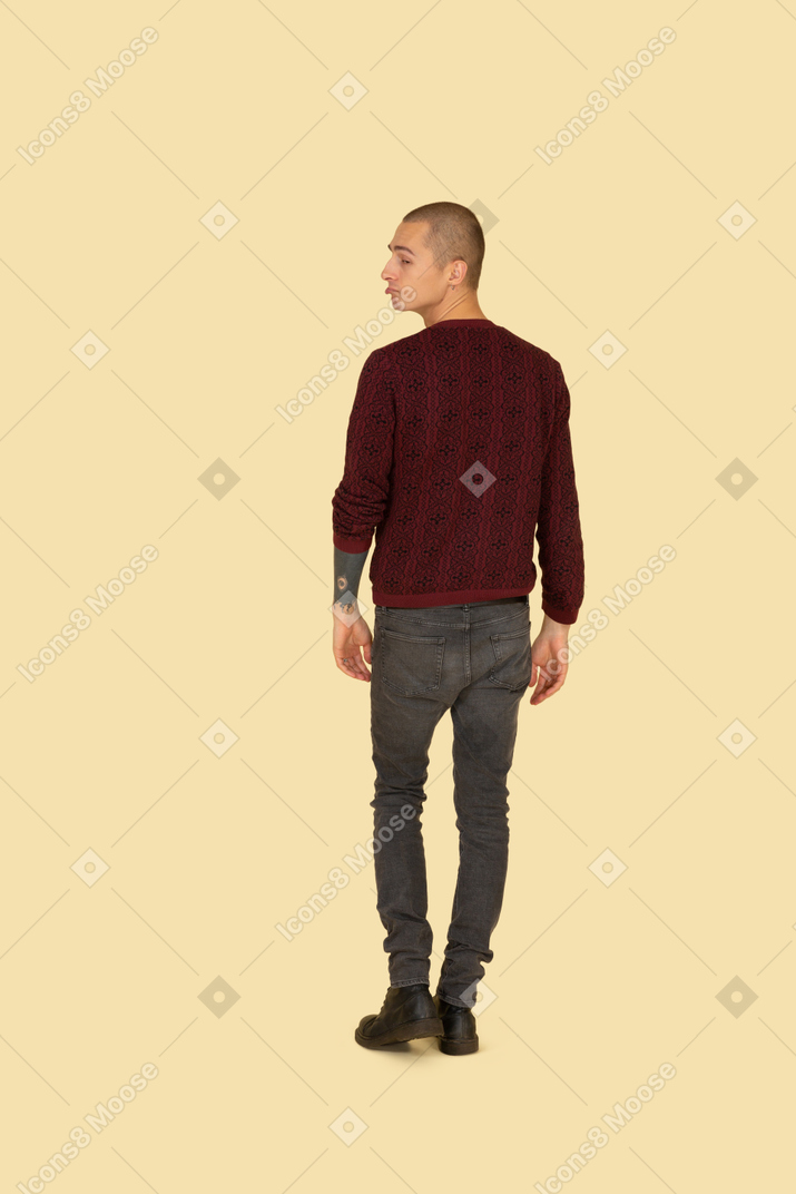 Back view of a grimacing young man in red pullover looking aside