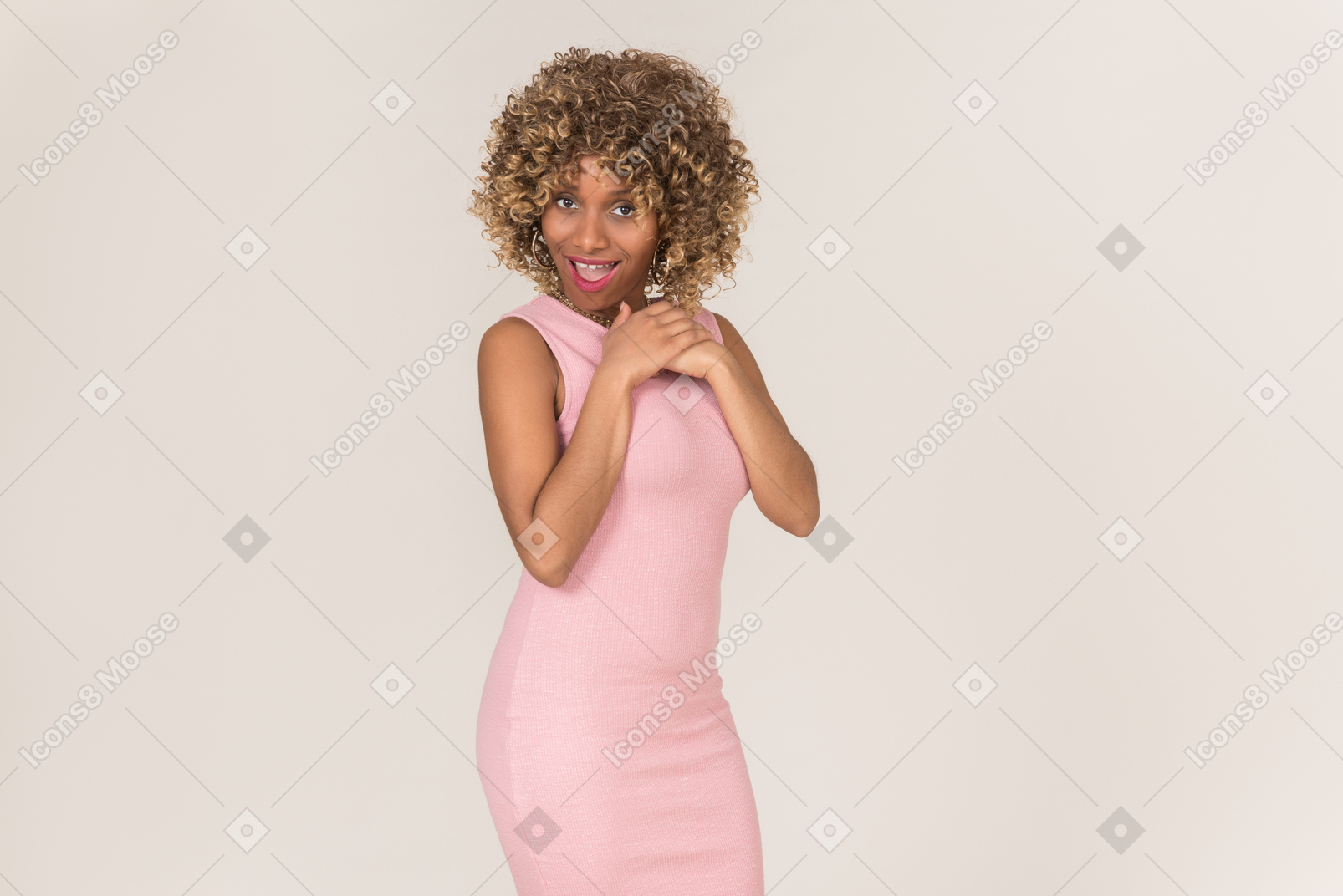 A young black fluffy-haired woman in a pastel pink dress, having fun alone against a plain grey background