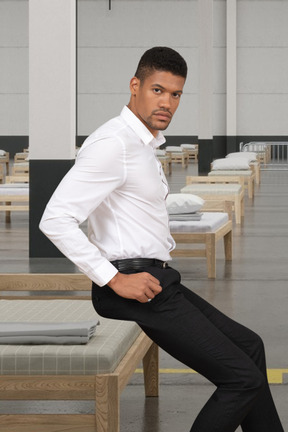 A man in a white shirt and black pants sitting on bed