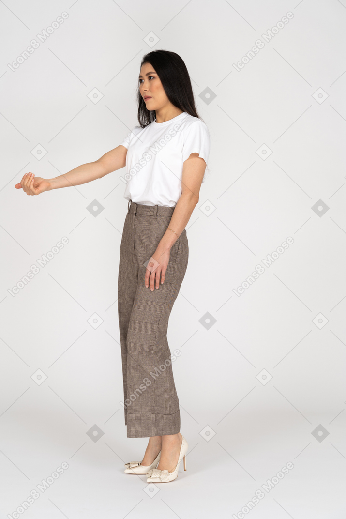 Vista di tre quarti di una giovane donna in calzoni e maglietta che tende la mano