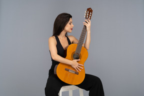 Front view of a sitting young lady in black suit looking at her guitar
