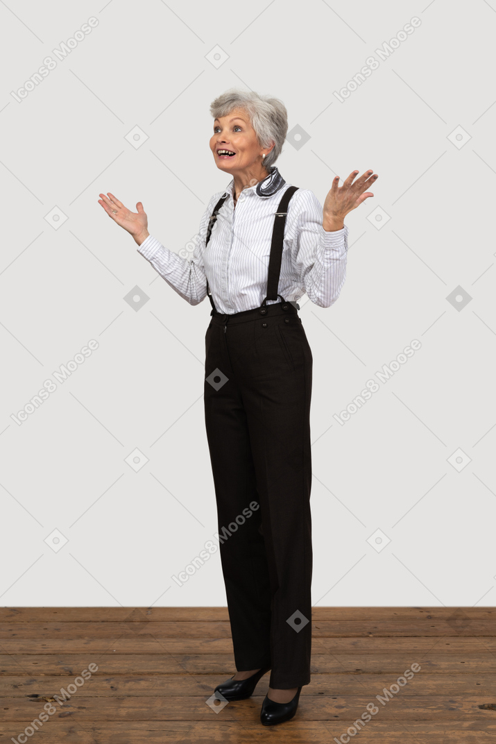 Three-quarters view of a surprised old female dressed in office clothes outspreading fingers and raising hands