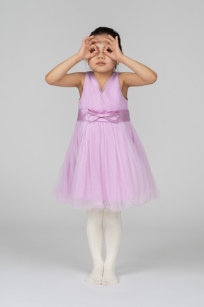 Маленькая девочка в розовом платье смотрит сквозь маску на палец