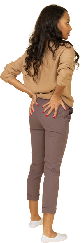 Vista posterior de tres cuartos de una mujer joven de piel oscura poniendo las manos en el trasero