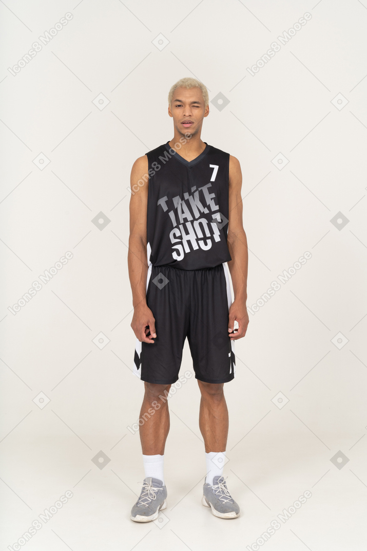 Vista frontal de um jovem jogador de basquete em pé com um olho aberto