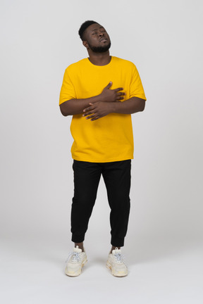 Vorderansicht eines jungen dunkelhäutigen mannes in gelbem t-shirt, das händchen auf dem bauch hält