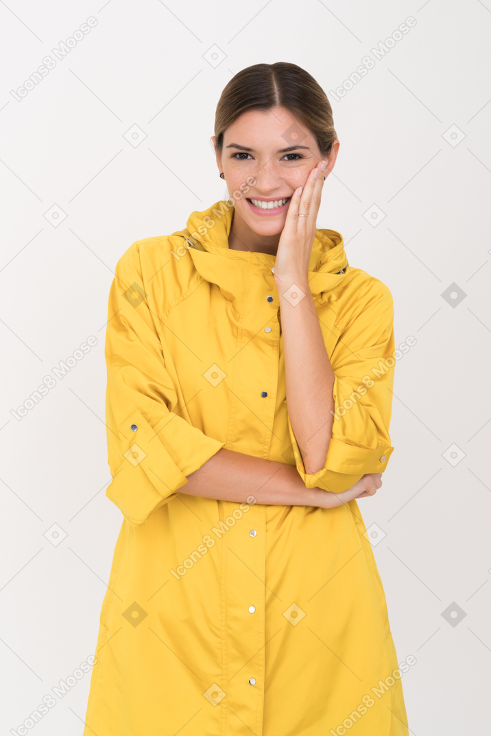 Jeune femme en imperméable jaune souriant et touchant sa joue avec un bras