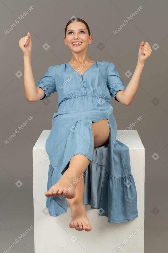 Front view of cheerful young woman sitting on cube and smiling