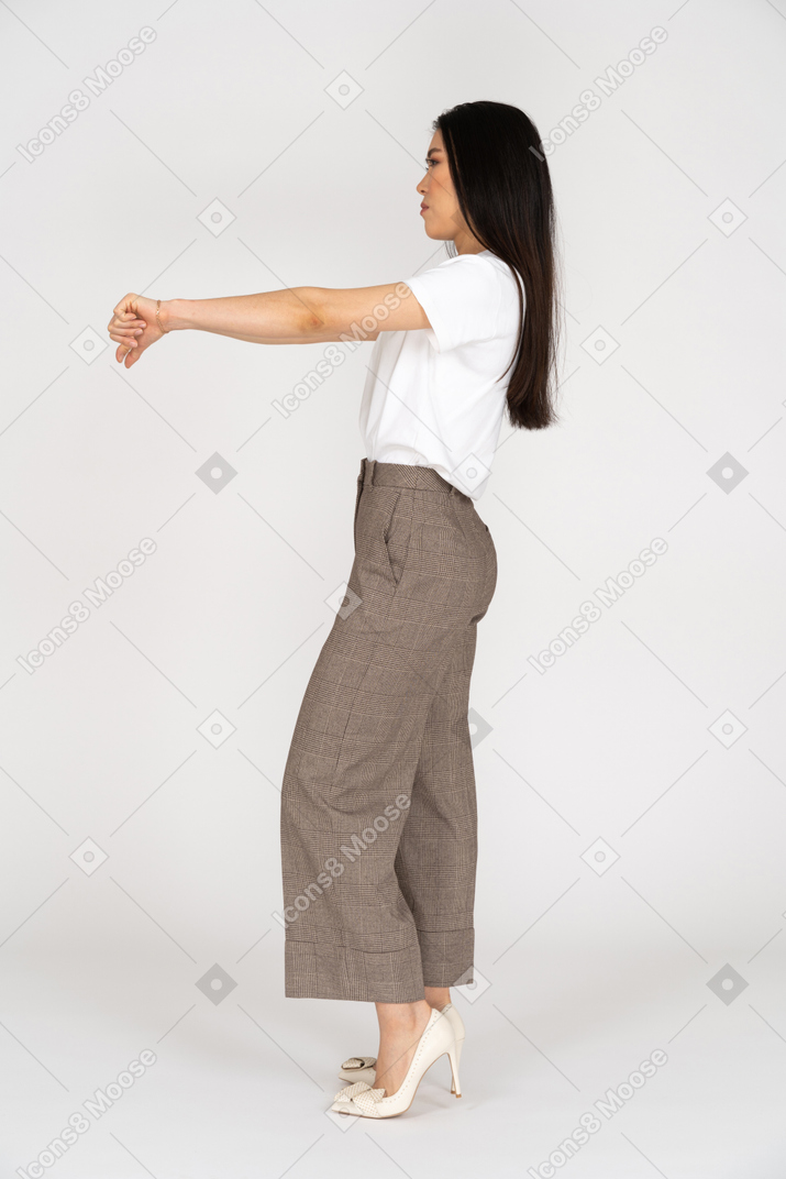 Вид сбоку молодой леди в бриджах и футболке показывает палец вниз