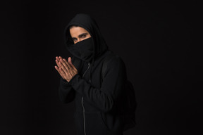 Hacker guy with covered face standing in the dark with hands folded