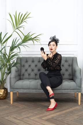 A woman sitting on a couch and touching up lipstick