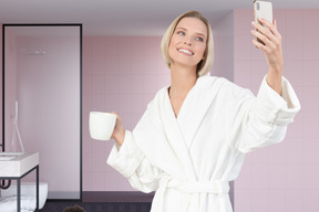 A woman in a bathrobe taking a selfie with her phone