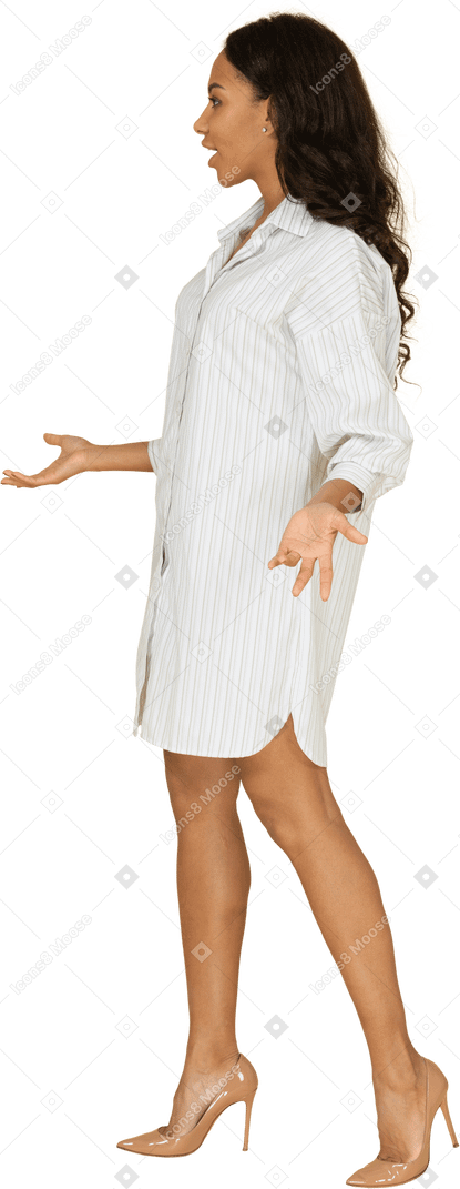Vista de tres cuartos de una mujer joven de piel oscura cuestionando en vestido blanco levantando las manos