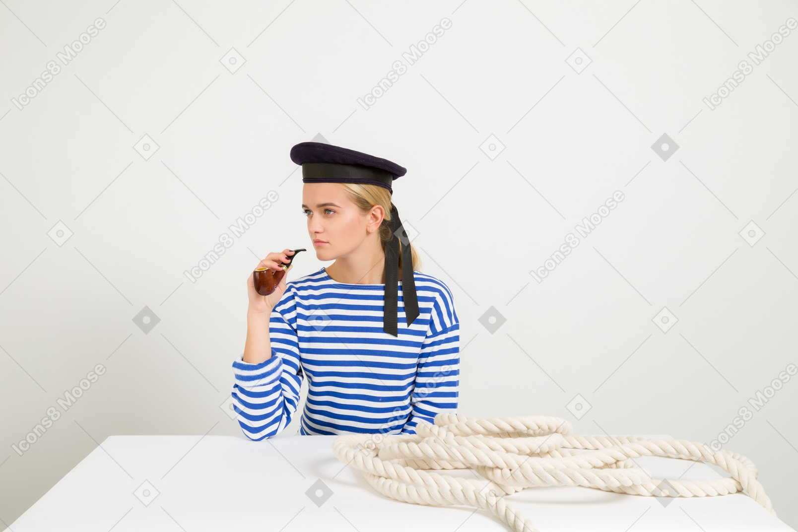 Marinero femenino sentado en la mesa con cuerda en ella y fumando pipa