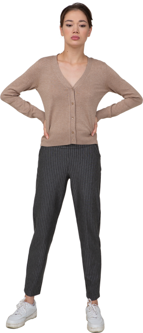 Vista frontale di una giovane donna in pullover e pantaloni che mette le mani sui fianchi