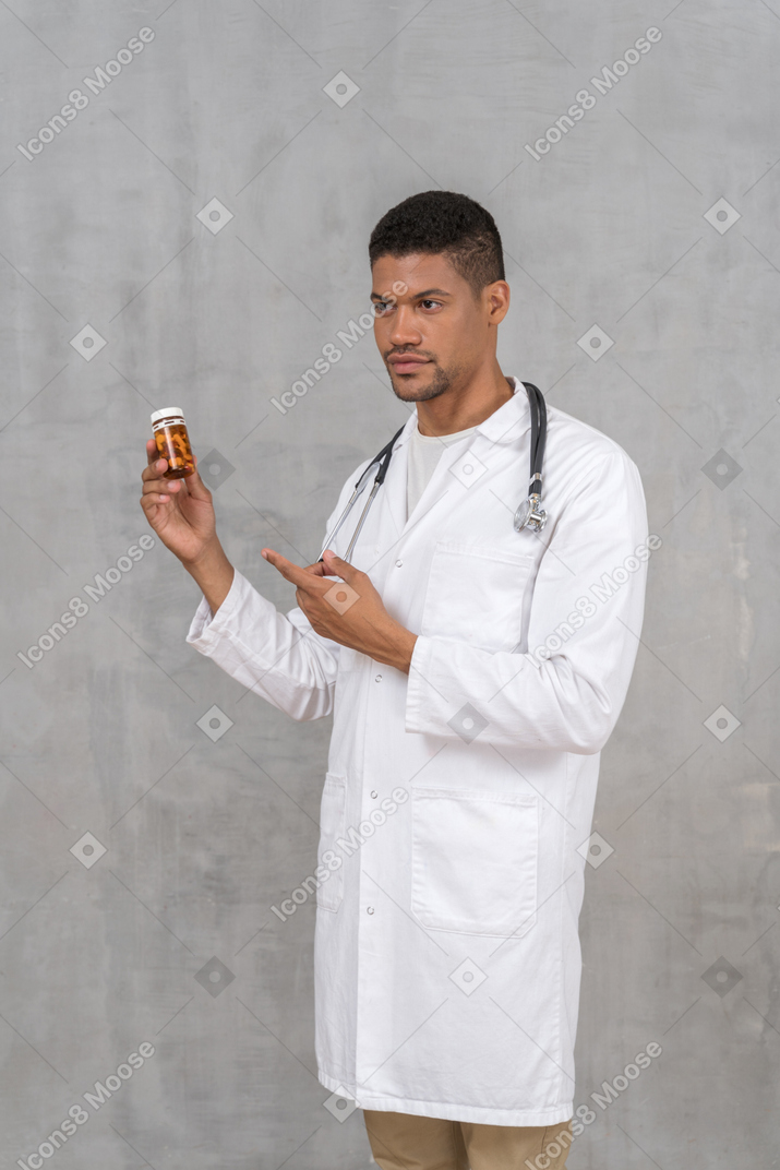 Young male doctor pointing at a pill bottle