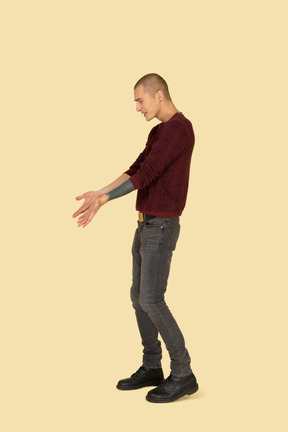 Side view of a young complaining man in red pullover outstretching his hands