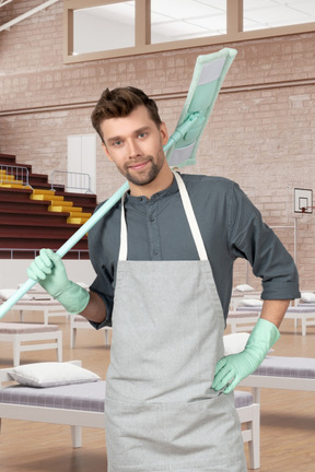 A man in an apron is holding a mop