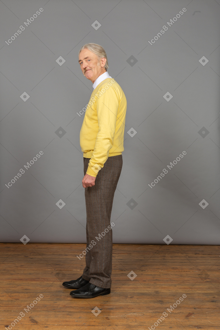 Side view of an old cheerful man in yellow pullover bending down and looking at camera while grimacing