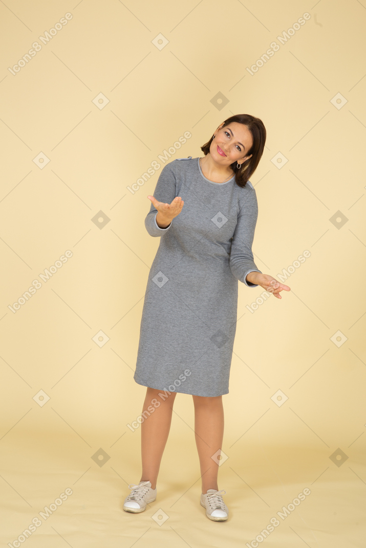Vista frontal de una mujer feliz en vestido gris mirando a la cámara