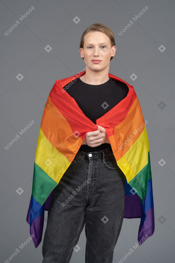 Nonbinary person standing wrapped in lgbtq+ flag