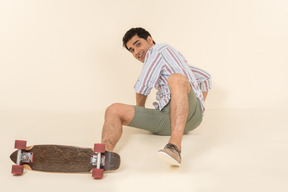 A nice-looking caucasian guy in a striped t-shirt, having fun learning how to ride a skateboard