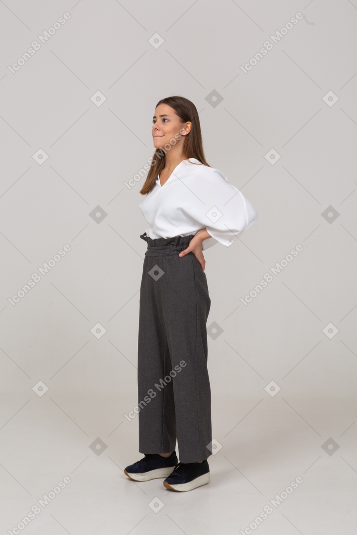 Vista de tres cuartos de una joven en ropa de oficina presionando los labios y poniendo las manos en las caderas