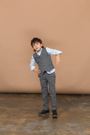 Вид спереди мальчика в сером костюме, стоящего с руками на бедрах