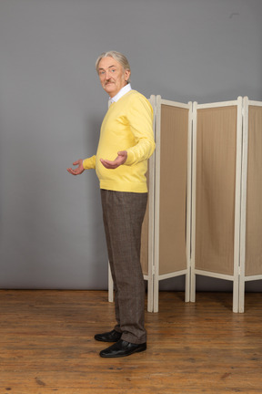 Side view of a perplexed old man raising hands looking at camera