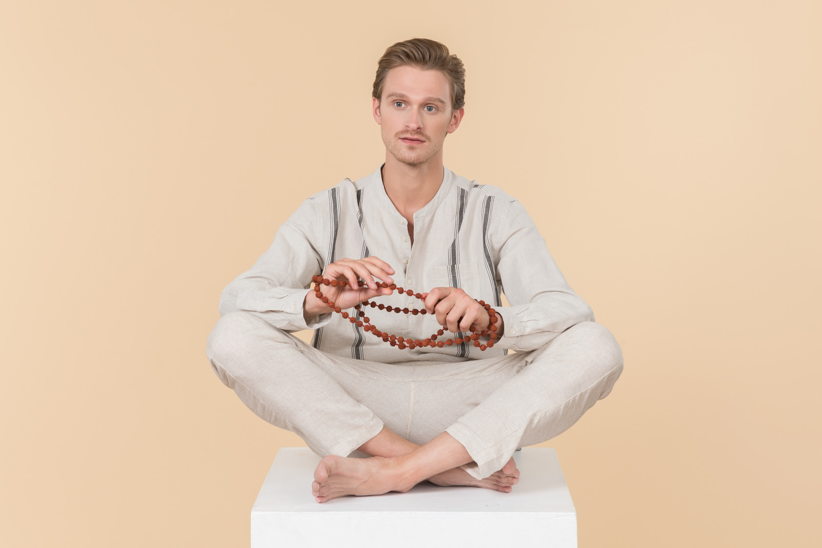 Young caucasian man sitting in lotus position and holding necklace